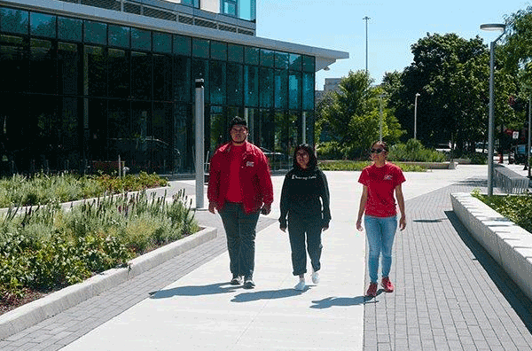 3 students walking through campus. 2 of them are Students Safety Escorts