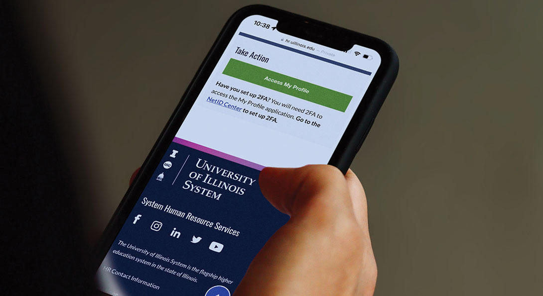 A hand holds a phone with the university of illinois system website on the screen