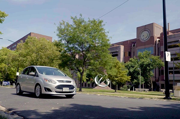 A silver car transiting on the street in front of the College of Nursing