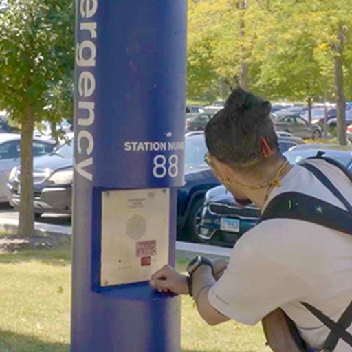 A student is talking through the callbox in a blue light pole at a campus arking lot