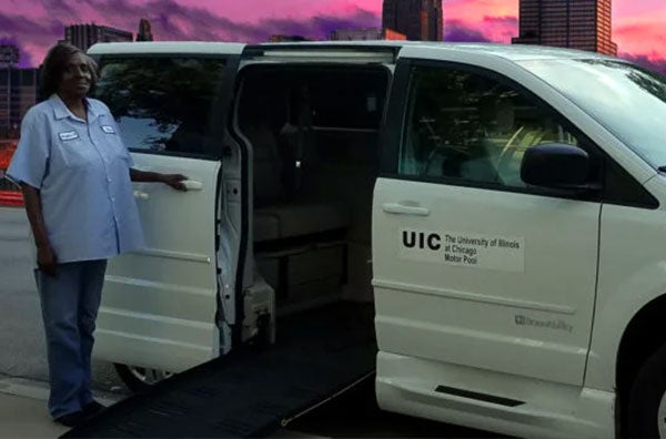 A UIC paratransit shuttle is parked with the ramp down and one staff member driver standing next to it