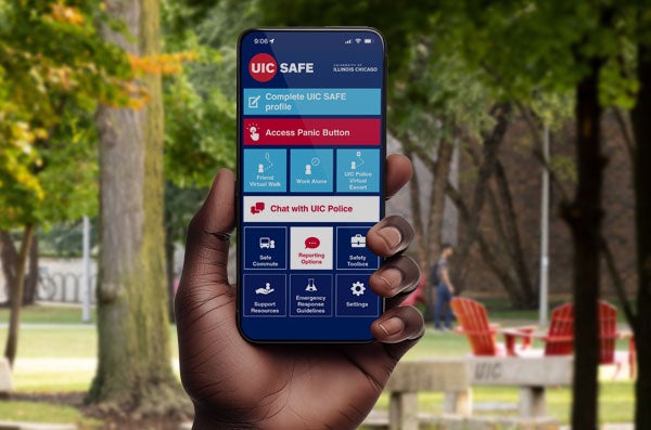 A hand holding a phone showing the screen with the UIC SAFE app