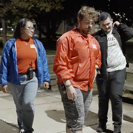 A male student is escorted through campus at night by two Student Patrol Officers