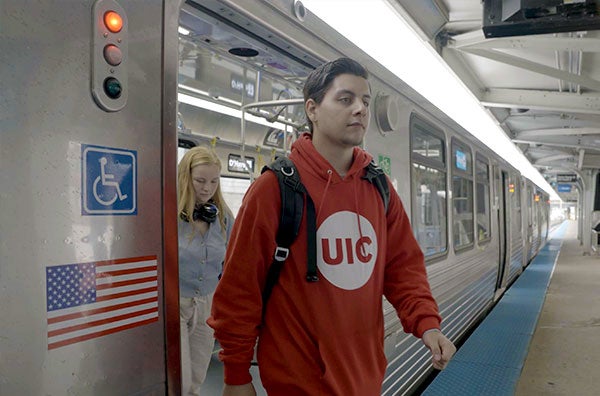 A male student wearing a red UIC hoodie is steping out of a train at the blue line