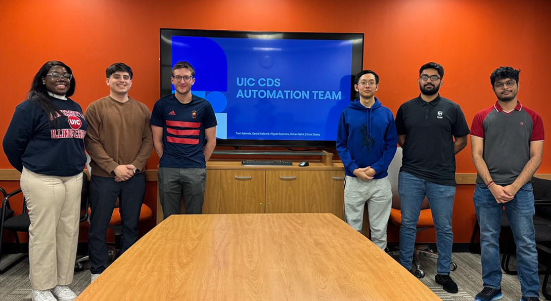 Six UIC students standing in a conference group in front of a wall screen that reads